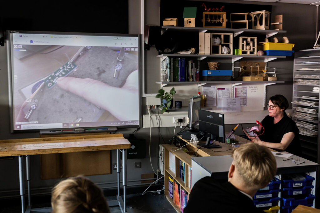 A photograph of design and technology teacher Victoria Stenholm teaching a about a small, complex electronic component. Using the HUE visualiser and a whiteboard she can manipulate the tiny component while everyone can see exactly what she's doing from their seats.
