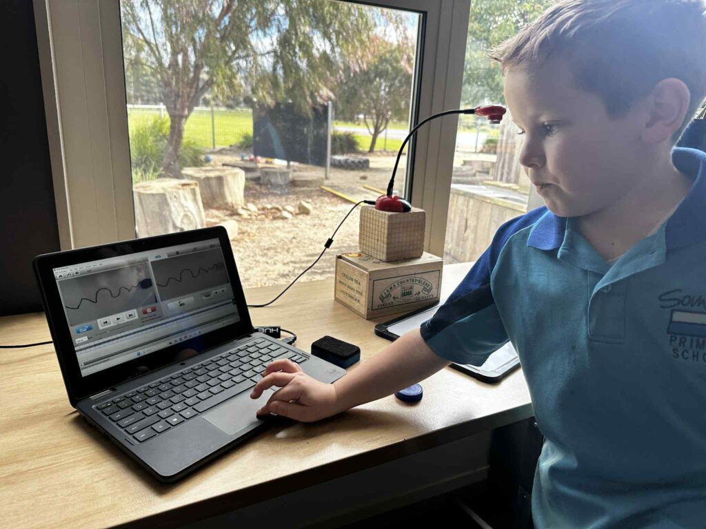 Photograph of a child with a laptop, using HUE Animation software and a HUE HD camera to create their very own stop motion animation project. They are seated at a desk and using household objects to raise the camera high above their 'film set'